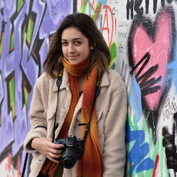 Veronica Backer-Peral with camera in front of graffiti wall